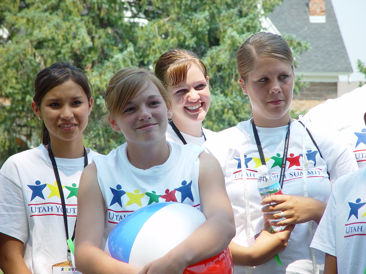 Four young people wearing Utah Youth Summit shirts stand outdoors with a beach ball.