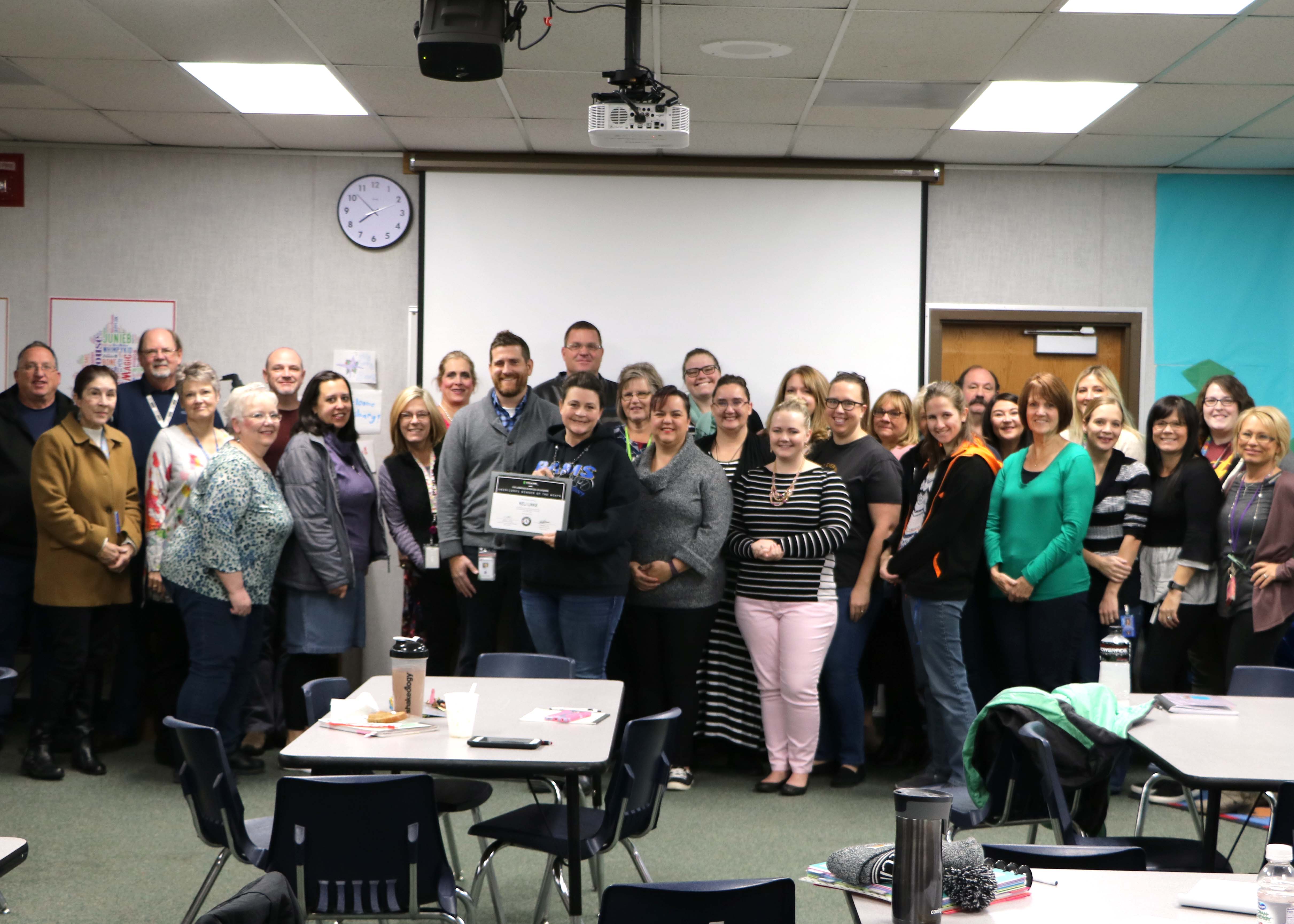 A group of adults poses together in a classroom, with one person holding a certificate.