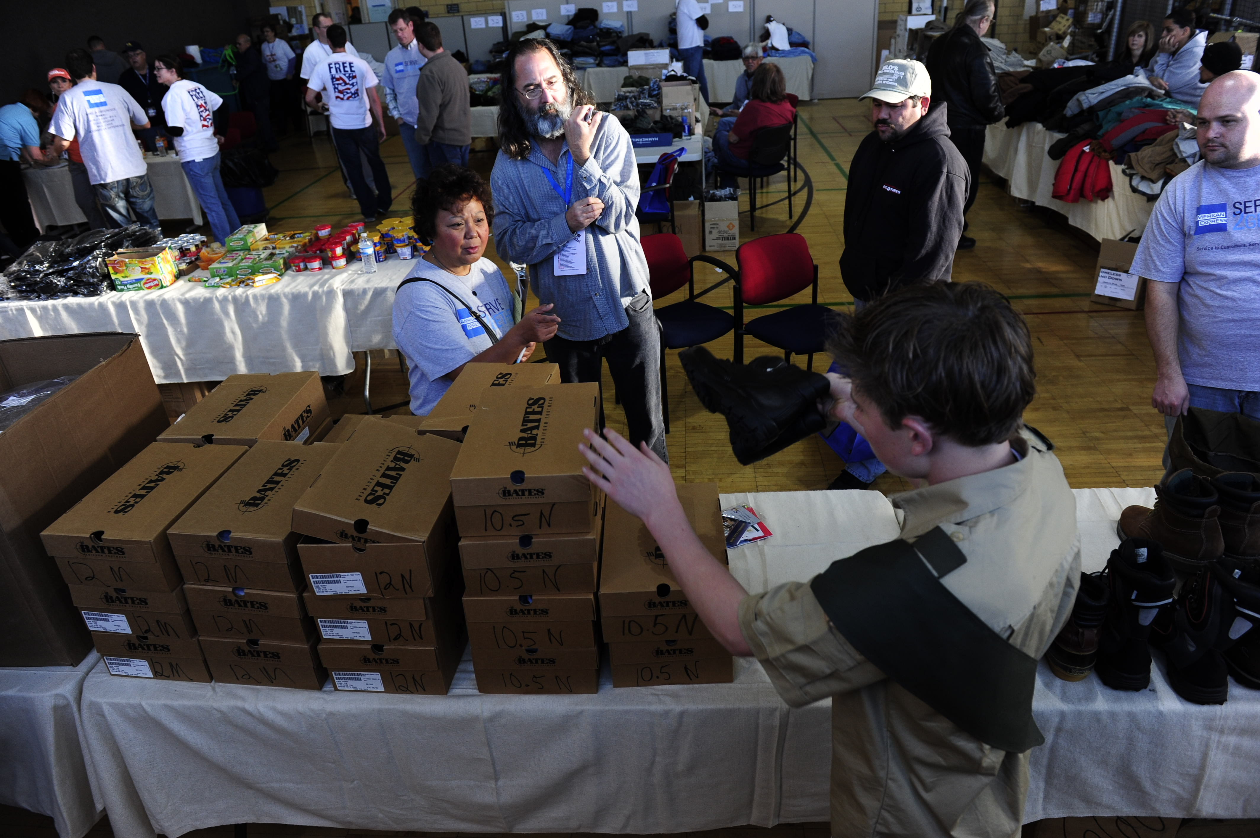 People distribute and receive shoe boxes at tables in a busy indoor event or donation drive.