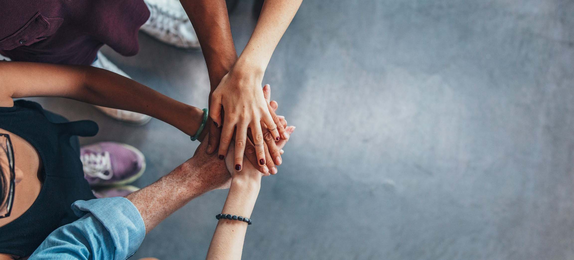 Several people stack their hands together in a gesture of teamwork, viewed from above.