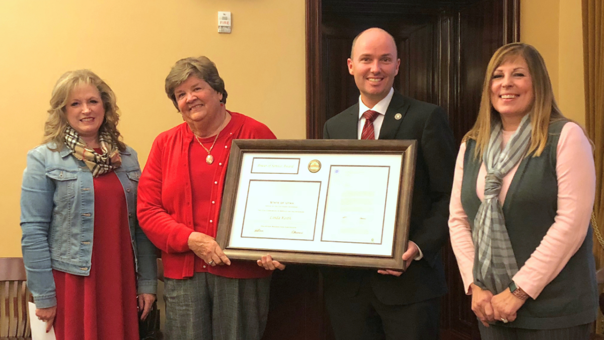 Debbie Hardy, Linda Keith, Lt. Governor Cox, and LaDawn Stoddard standing in capitol board room holding large framed award.