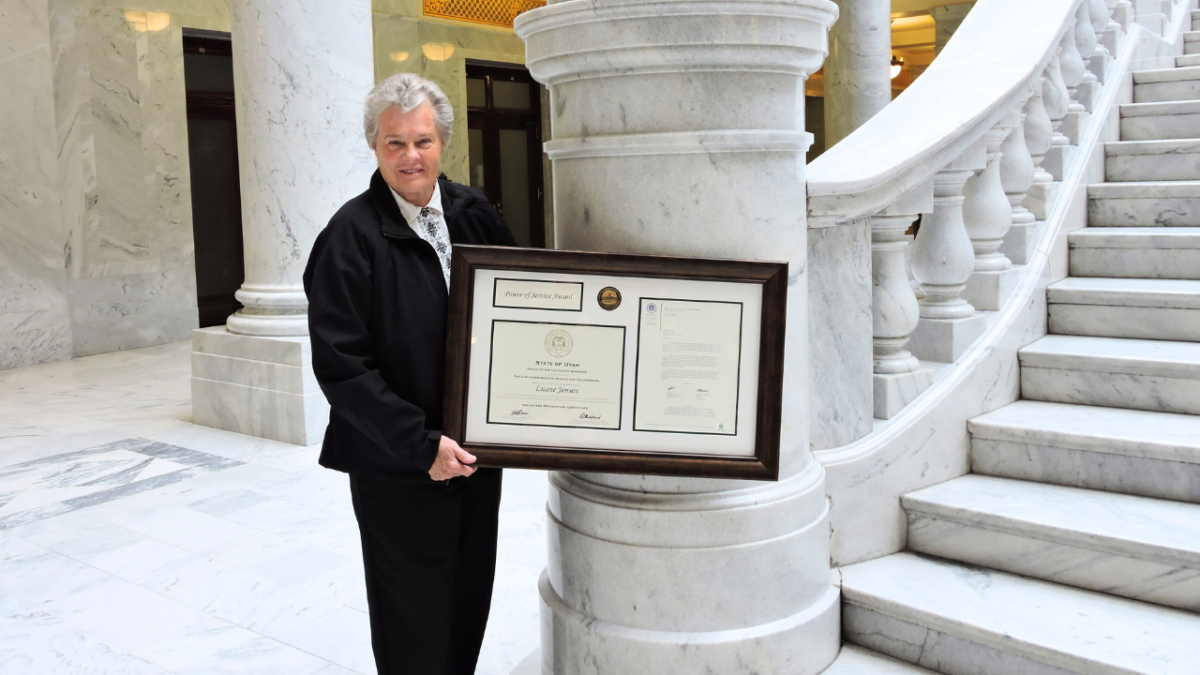 Luane Jensen standing in front of interior capitol stairs holding large framed award.