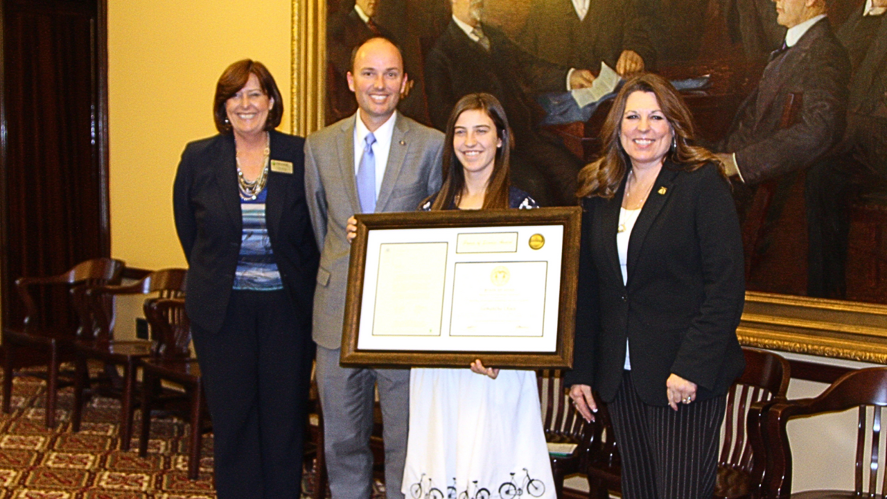 Individuals standing in Capitol Board Room holding large framed award.