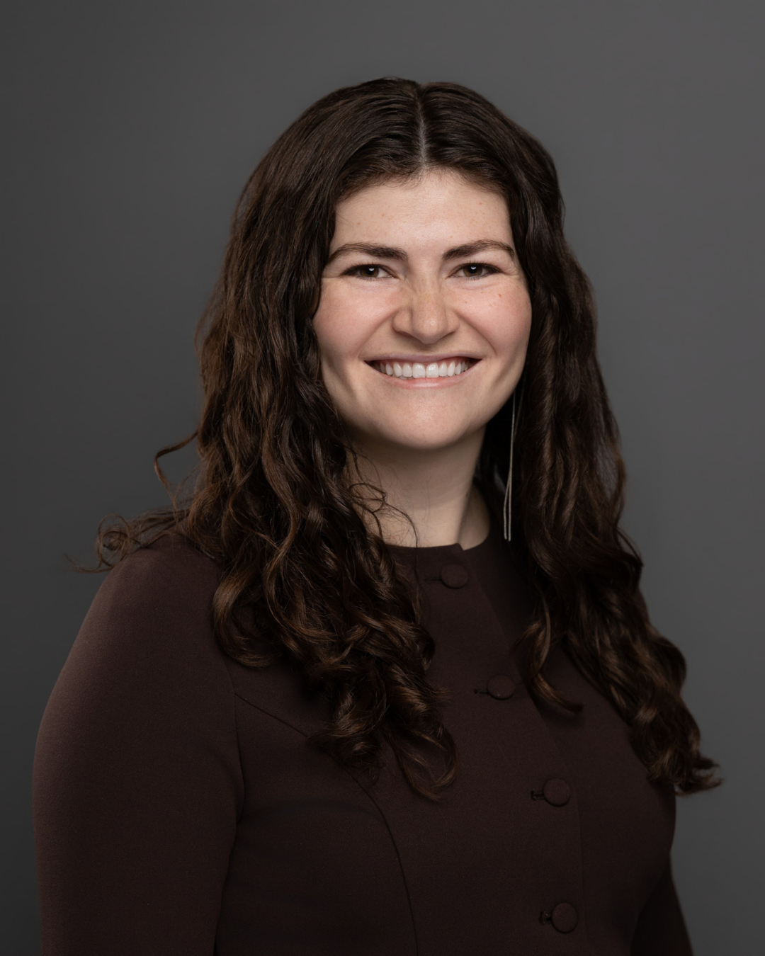 Young woman with long dark hair smiling at camera wearing black shirt in front of dark gray background