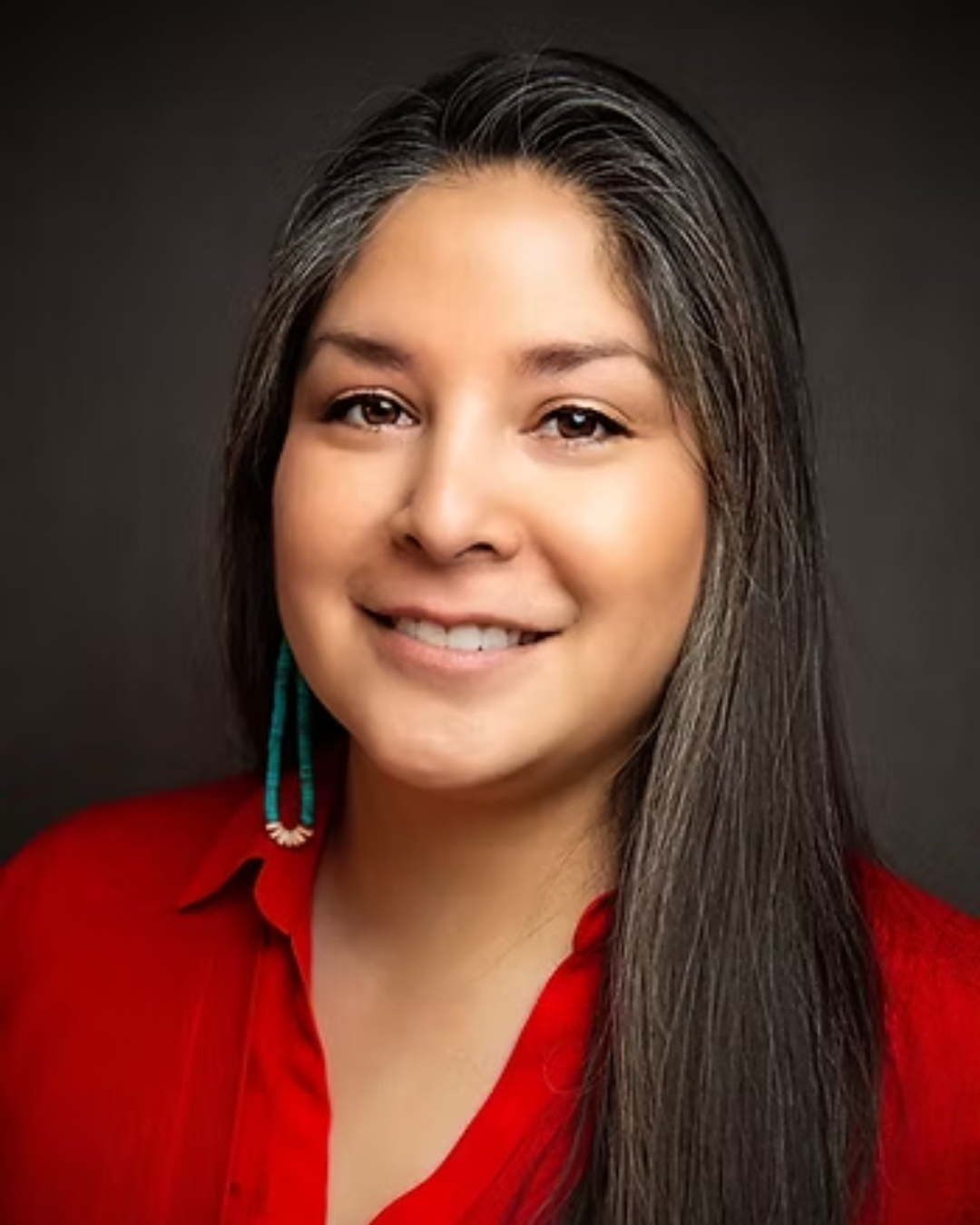 Woman with long dark hair smiles at camera wearing red collared shirt in front of dark gray background