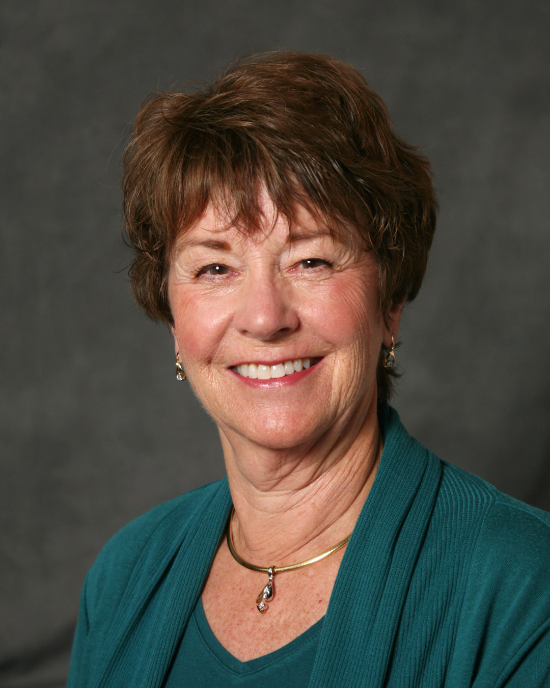 Woman with short brown hair smiling at camera in front of dark gray background