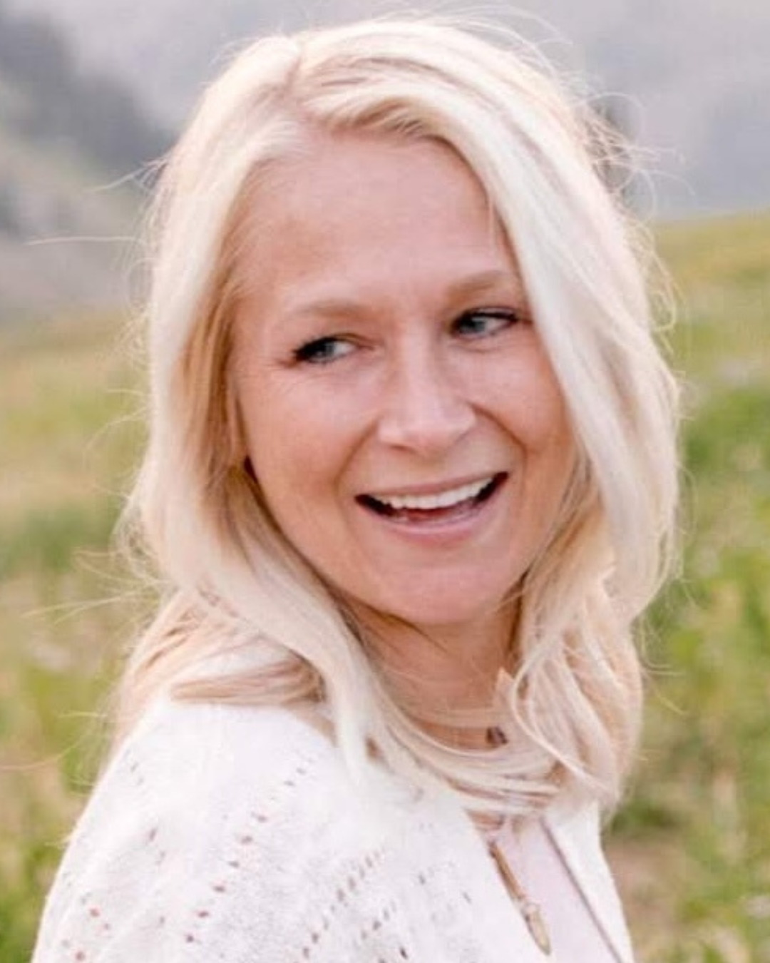 Woman with shoulder length blonde hair smiles in outdoor setting