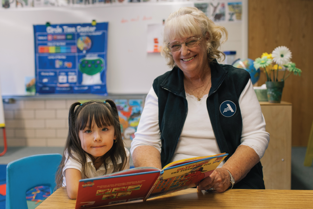 Foster Grandparent volunteer reading a book with a student in a classroom