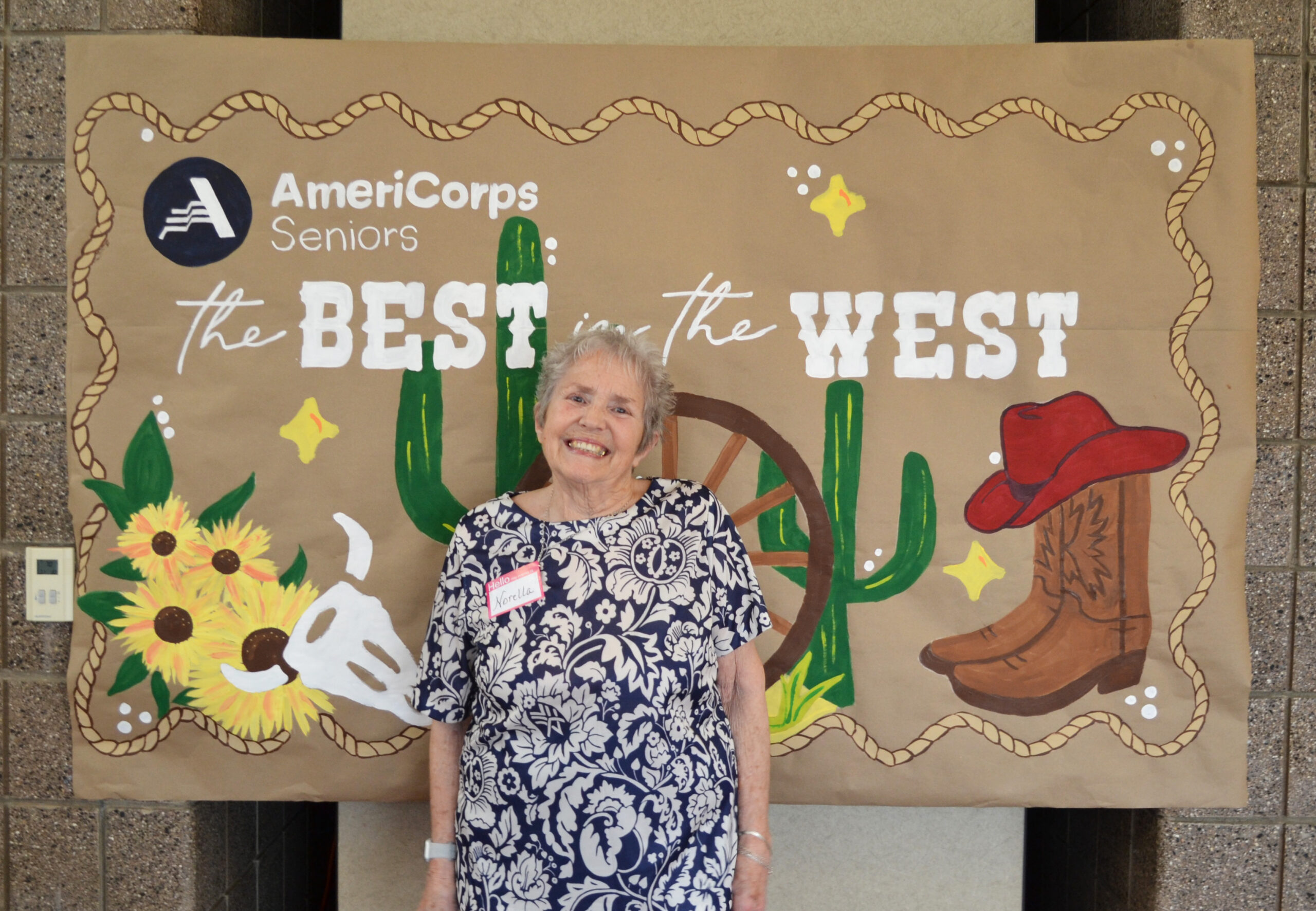Elderly woman smiling in front of a Western-themed AmeriCorps Seniors event backdrop.