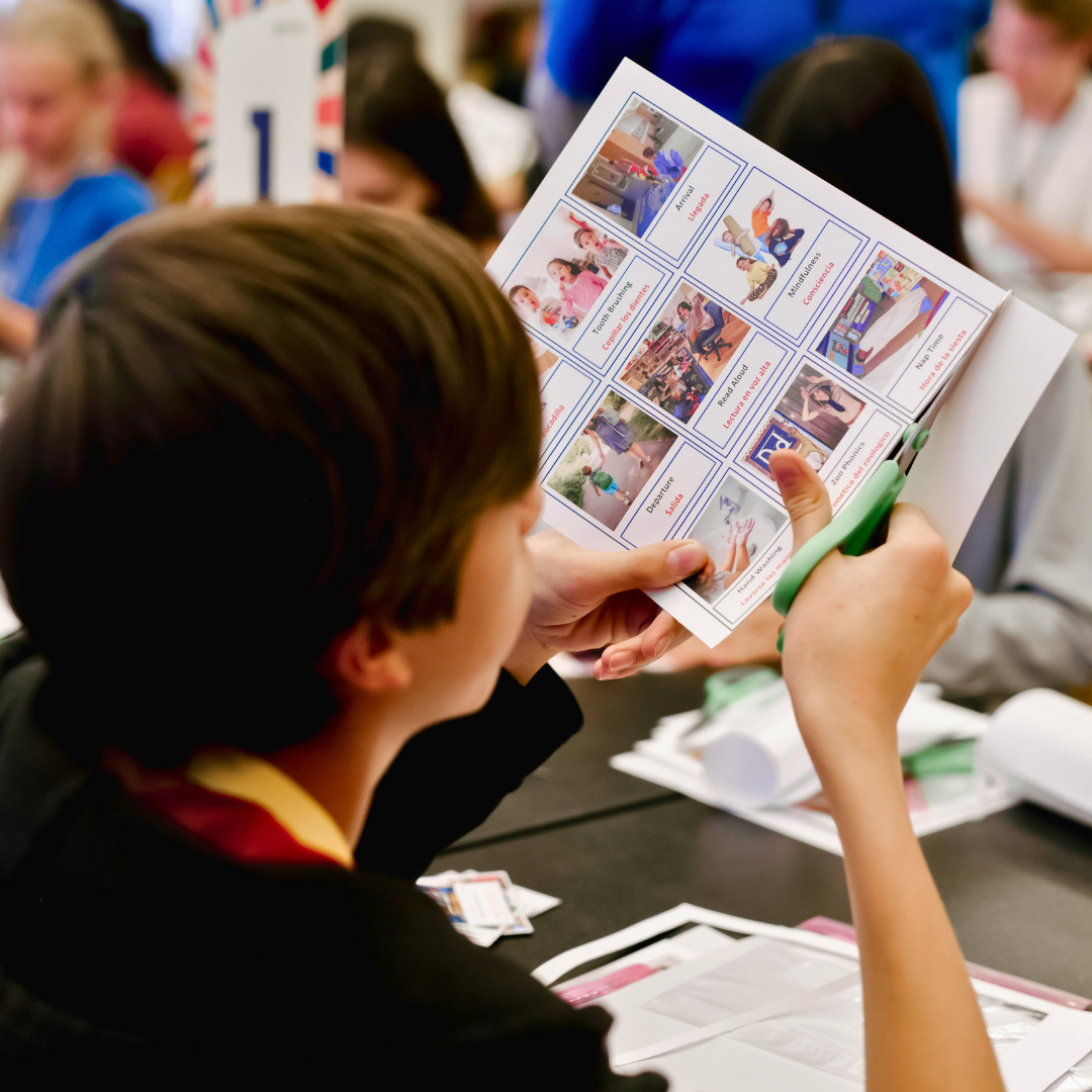 Person cutting a sheet of pictures with scissors at a table in a group setting.